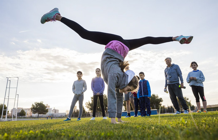Young girl doing gymnastics on a field in front of classmates (photo)